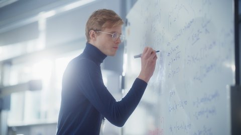 Education, Learning, Mathematics Concept: Young Male Specialist Write Formulas and Solving Problems Behind the Whiteboard in Bright Modern Laboratory