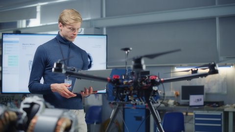 Male Developer Works on Engineering Project, Code at Laptop and Look at Drone at Modern Office. Empowered Person Creating Unmanned Aerial Vehicle Concept. Portrait View