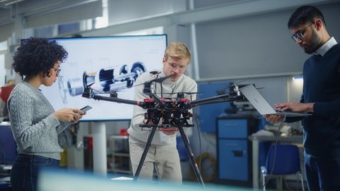 Young Engineers Create Innovative Program for Drones at Modern Scientific Laboratory. Team of Aviation Specialists Work on a New Drone, Have Discussion, Use Laptop and Tablet
