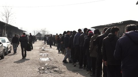 Hundreds of refugees are standing in line for food donation in a temporary refugee camp, during the European refugee crisis. some volunteers are visible among them. Feb 22nd, 2017, Belgrade, Serbia.
