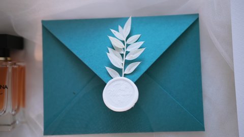 An exquisite envelope made of expensive textured paper is decorated with wax stamp and twig with leaves. Word wedding is written on seal. Stationery decor elements. Envelope for invitation and letter
