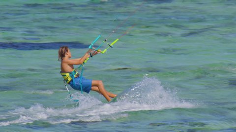 Young kiteboarder surfing in Mauritius jumps while riding around the turquoise lagoon. Kitesurfer splashes glassy ocean water while riding in Mauritius