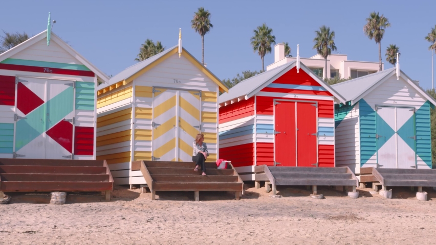 A lady sitting on the steps of one of the iconic brightly painted beach hut on Brighton Beach Victoria