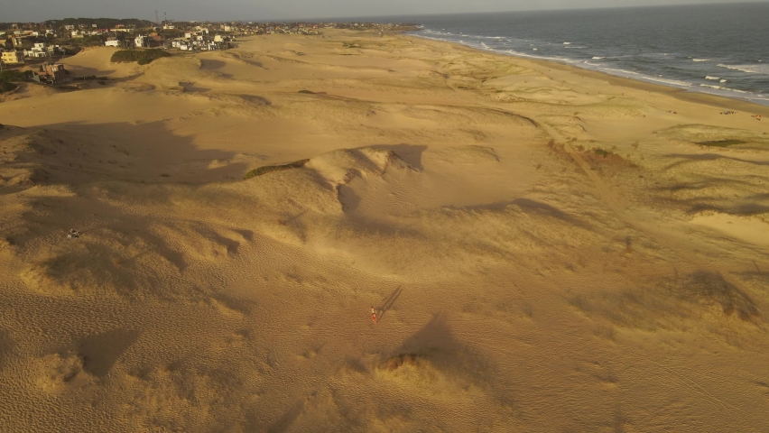 wide drone shot of a Couple walking beach by dunes at sunset. Romantic moments on sandy beaches. Playa La Viuda in Uruguay Royalty-Free Stock Footage #1090200227