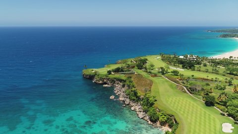 Tropical peninsula with golf course and palm sandy beach, top view. Grass lawn and forest trees in a tropical summer park. Sunny Caribbean coast. Blue lagoon near the rocky seashore. Seascape.