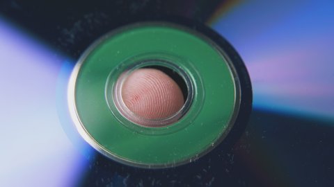 modern shining compact disk on young person finger with grooves on blurred dark background extreme close view