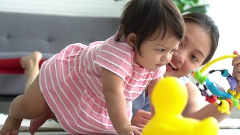 A 7-month-old baby girl is interested in a toy that an Asian mother brings to her, which is a baby learning to crawl, to baby children and development concept.