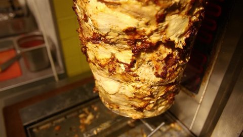 Skewered roasted chicken shawarma meat cooking and turning on rotating spit in fast food restaurant. Turkish traditional cousin.