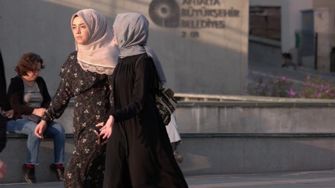 Antalya, Turkey - 02.11.2019: Two young Muslim women in hijab walking on city street. Many people outdoors on a summer day.