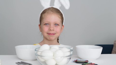 Curious little girl in bunny ears is going to paint eggs for Easter. Happy Easter holiday. Eggs, Easter Bunny - a symbol of the holiday Easter.