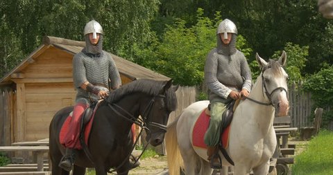 KIEV/UKRAINE - AUG 17 2014: Two Actors, Horsemen, Knights, mid shot, Brown And White Horses, horsemem are in Chain Armors and Helmets, green and pink pants, horses are chewing, wooden fence,