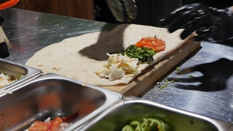 culinary tongs put chopped vegetables and greens dill and cilantro on pita bread in the process of cooking lula kebab or doner kebab. Cook's hands add ingredients for shish kebab on pita bread