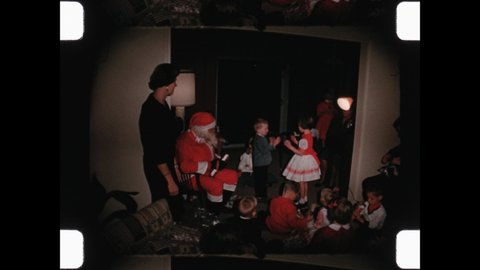 1963 Orlando, FL. Mother and man in  Santa Clause suit look on as children play patty cake and dance at holiday party for kids. Kids celebrate at holiday party. 4K Overscan of Vintage Home Movie