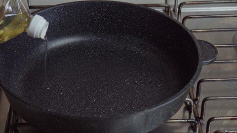 Cook pours sunflower oil into a frying pan. Kitchen pan stands on Stove and oil is poured into it for frying. Oil is pouring into the pan. High quality 4k footage