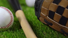 A slider shot over a black wooden bat, past a brown and black leather baseball glove and numerous new baseballs along sitting on the turf stopping at a select one, ready for practice. - Powered by Shutterstock - Get 15% off with code: PIKWIZARD15