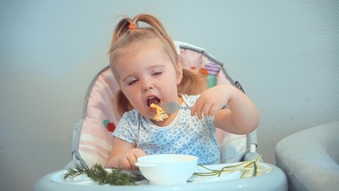 Funny Cute Little Children Sitting In Chair Kindergarten Eating Supplementary Healthy Food For Toddlers. Adorable Happy Infant Baby Eating. Cute Child Little Girl Eating Healthy Food In Kindergarten. 