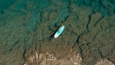 Aerial view: Man paddling on a stand up board on turquoise water. People on vacation in Croatia enjoying water sport 