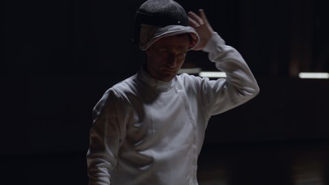 Portrait of Caucasian male fencer putting on his protective helmet, getting ready for the fight