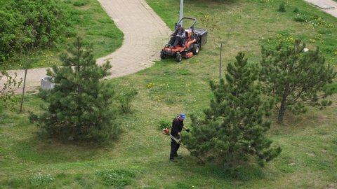 Pruszcz Gdanski, Gdansk, Poland - May 13, 2022: Men cutting green spring grass growing on lawn in city. Aerial top view 4k video footage of adult men mowing lawns with lawn mowers