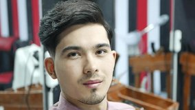 Stylish young guy is sitting in a barber shop. Barber making a fashionable haircut