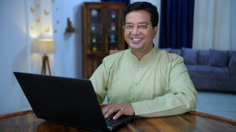 A handsome Bengali businessman doing his office work on his laptop - a remote job, COVID-19 lifestyle . An attractive male wearing a colorful Kurta happily posing for the camera while taking a break.