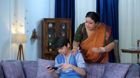 A strict Indian mother scolding her son for excessive mobile use - technology overuse, mobile addiction. A young teenage boy and her mother - angry mother, upset boy