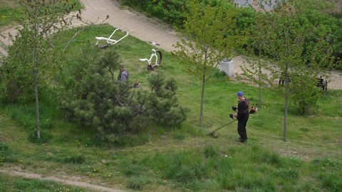 Pruszcz Gdanski, Gdansk, Poland - May 13, 2022: Men cutting green spring grass growing on lawn in city. Aerial top view 4k video footage of 2 adult men workers mow lawns with lawn mower