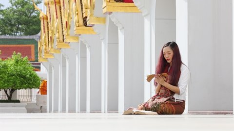 Asian buddhist woman reading Lanna Sanskrit ancient palm leaf manuscript of Tripitaka the Lord Buddha dhamma teaching while sitting in temple on holy full moon day to chant and worship in monastery