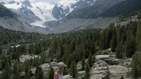 Drone view of female mountain climber rappelling on rock face. Aerial view of sporty woman rock climbing in summer in an alpine climate in the Swiss Alps, glacier on the background.