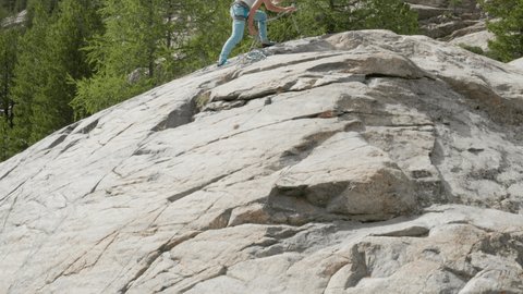 Drone view of female mountain climber rappelling on rock face. Aerial view of sporty woman rock climbing in summer in an alpine climate in the Swiss Alps