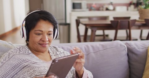 African american senior woman wearing headphones using digital tablet sitting on the couch at home. retirement lifestyle living concept