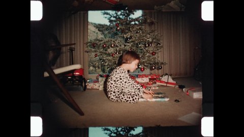 1967 Phoenix, AZ. Brother and Sister open gifts Christmas morning while Mom in her bathrobe cleans up the mess. Wrapped Presents under the Christmas Tree. 4K Overscan of Vintage Home Movies Redaksjonell arkivvideo