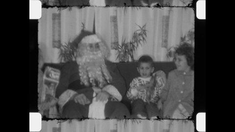 1953 Chicago, IL. Santa Claus brings Gifts to children. Brother and Sisters sit on sofa with St. Nick. Man in fake beard and Santa suit entertains kids on Christmas Eve. 4K Overscan of Home Movies