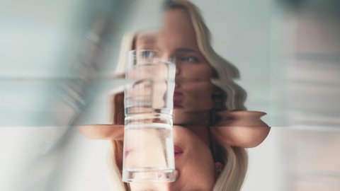 Surreal portrait. Contemporary face. Mirror distortion. Boomerang motion. Creative visual illusion of woman blinking eyes in water glass reflection GIF loop.