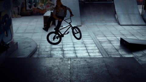 Teenage bmx rider performing dangerous jump stunt trick at urban skate park. Active man in casual clothing racing up on bmx bicycle outdoors. Extreme hobby active lifestyle urban subculture concept.