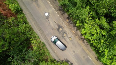 PANAMA, MAY 2021, AERIAL TOP DOWN: Car driver handling big potholes on countryside road in tropics. Bending paved road and careful road pits bypassing along exotic countryside.
