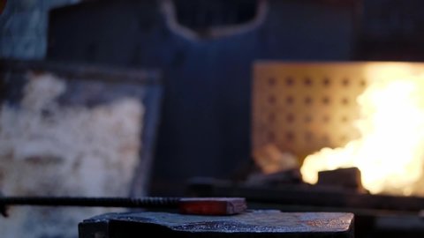 Cinematic style of a blacksmith in slow motion forging a hot iron in the forge. Craftsmanship in antique works with fire in the background.