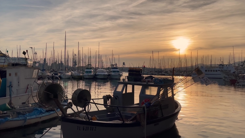 South of France, Toulon Port on mediterranean sea, with an old fishing boat and sailing boats. Harbour view during the sunset (or sunrise) with big gold sun and orange sky.