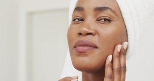 Video of happy african american woman in robe moisturizing face. beauty treatment and skin care routine concept.