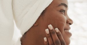 Video of happy african american woman in robe moisturizing face. beauty treatment and skin care routine concept.