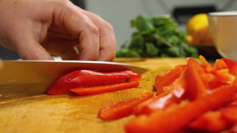 Close-up of a woman's hands with a knife cutting red bell peppers on a kitchen board. Vegetarian Kitchen. In the background a bunch of parsley. Slow motion. The concept of delicious and healthy food