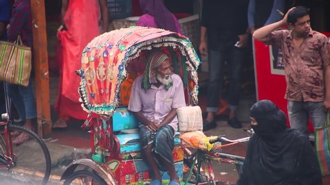 Faridpur, Bangladesh- May 15, 2022: In the rain, a rickshaw puller sits on a rickshaw looking for passengers.
