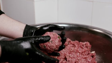 Close up shot of making buger form meatballs by the chef in the kitchen. Chef wearing black gloves forming burger patty.