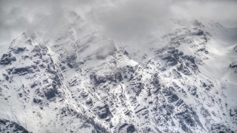 8K 7680X4320.Clouds on snowy rocky sharp mountain peaks.Scary creepy high altitude summit.Cliff and a depressing mountain wall.HDR Time lapse nature.Winter peak summit slope ridge topography geography