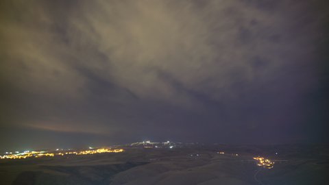 8K 7680X4320.Stars and starry night lights in partly cloudy sky.Lights of tv transmitter antennas on mountain peak.Brown fields on treeless hills.Ground time lapse background cloud.Treeless hill dark.