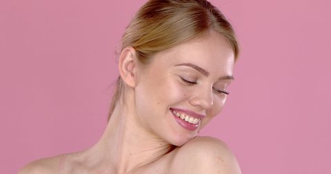 Slow motion video shot of smiling beautiful girl, isolated on pink background. Bare shoulders