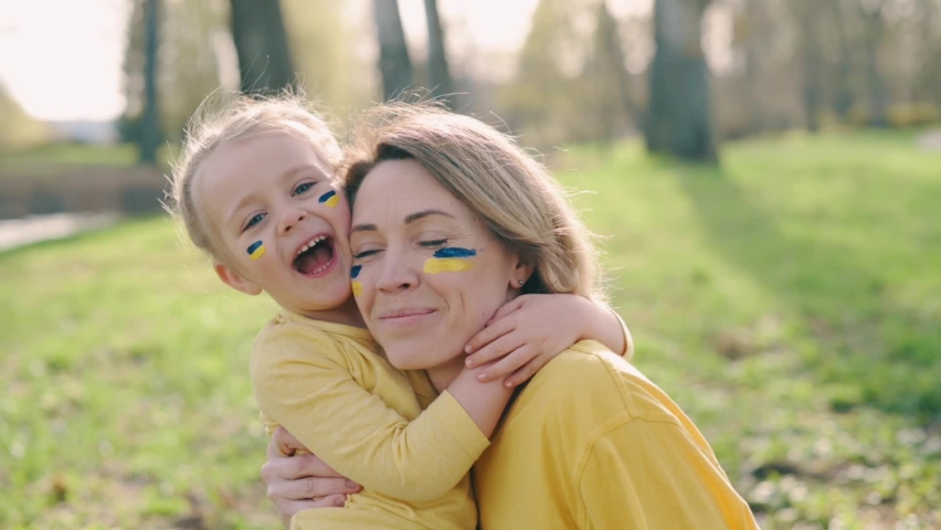 Portrait of Ukrainian family. Mom with two little daughters with painted flags of Ukraine on their faces look at camera. Close up. | Shutterstock HD Video #1090248201