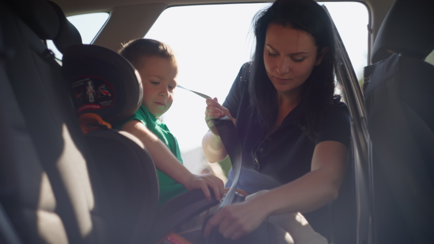 The boy gets into the car seat. Mom fastens the child in the car seat. High quality 4k footage Royalty-Free Stock Footage #1090250215