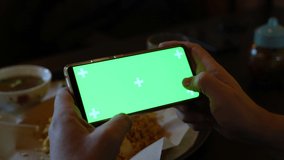 Man playing video game with green screen on smartphone at cafe. Male in cafe using movile phone viewing green screen press browsing chroma key online typing text reading social media close up hands