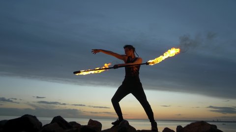 A young guy puts on a fire show against the backdrop of a sunset sky and a river